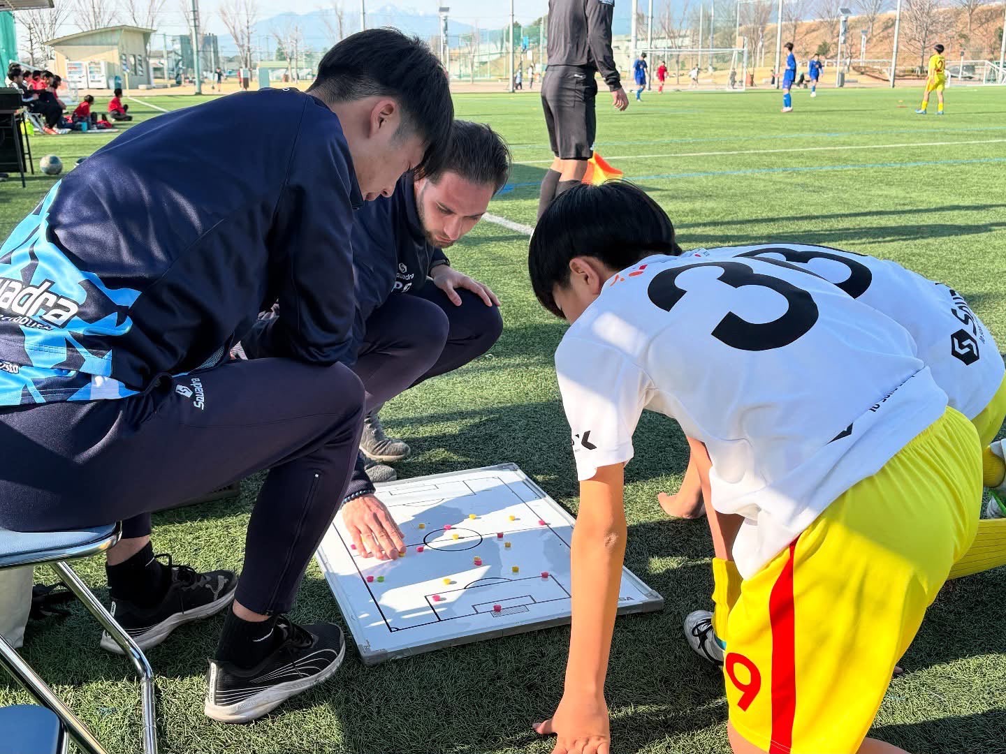 Coaching staff and a player crouched over a magnetic tactics board on the touchline